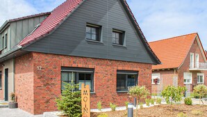 Una casa moderna de dos pisos con techo gris oscuro y fachada de ladrillo rojo.