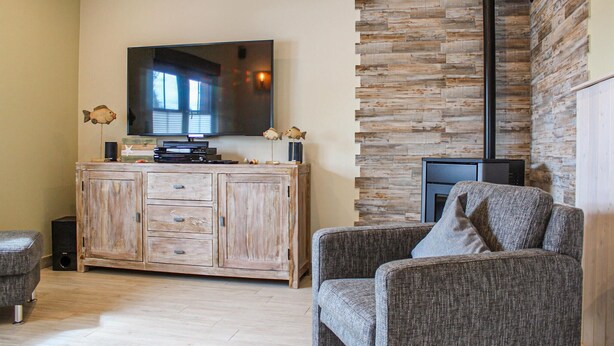 Una sala de estar con un mueble de madera, un televisor de pantalla plana, peces decorativos, una chimenea y un sofá gris.