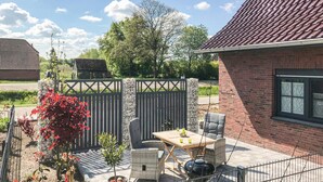 Un patio con mobiliario exterior, una parrilla y un jardín cercado.