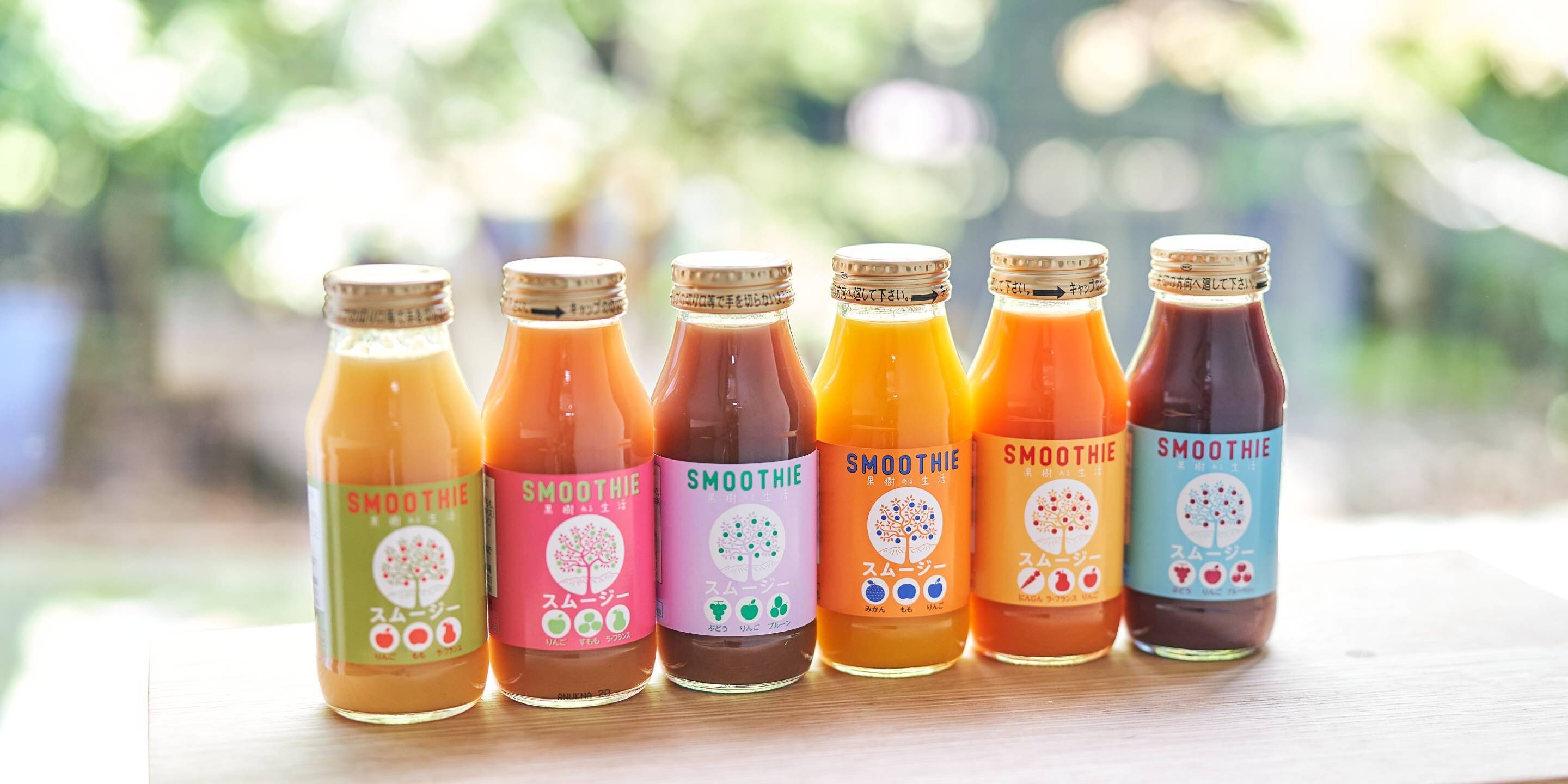 Six bottles of smoothie with different colors and labels, arranged on a wooden surface.
