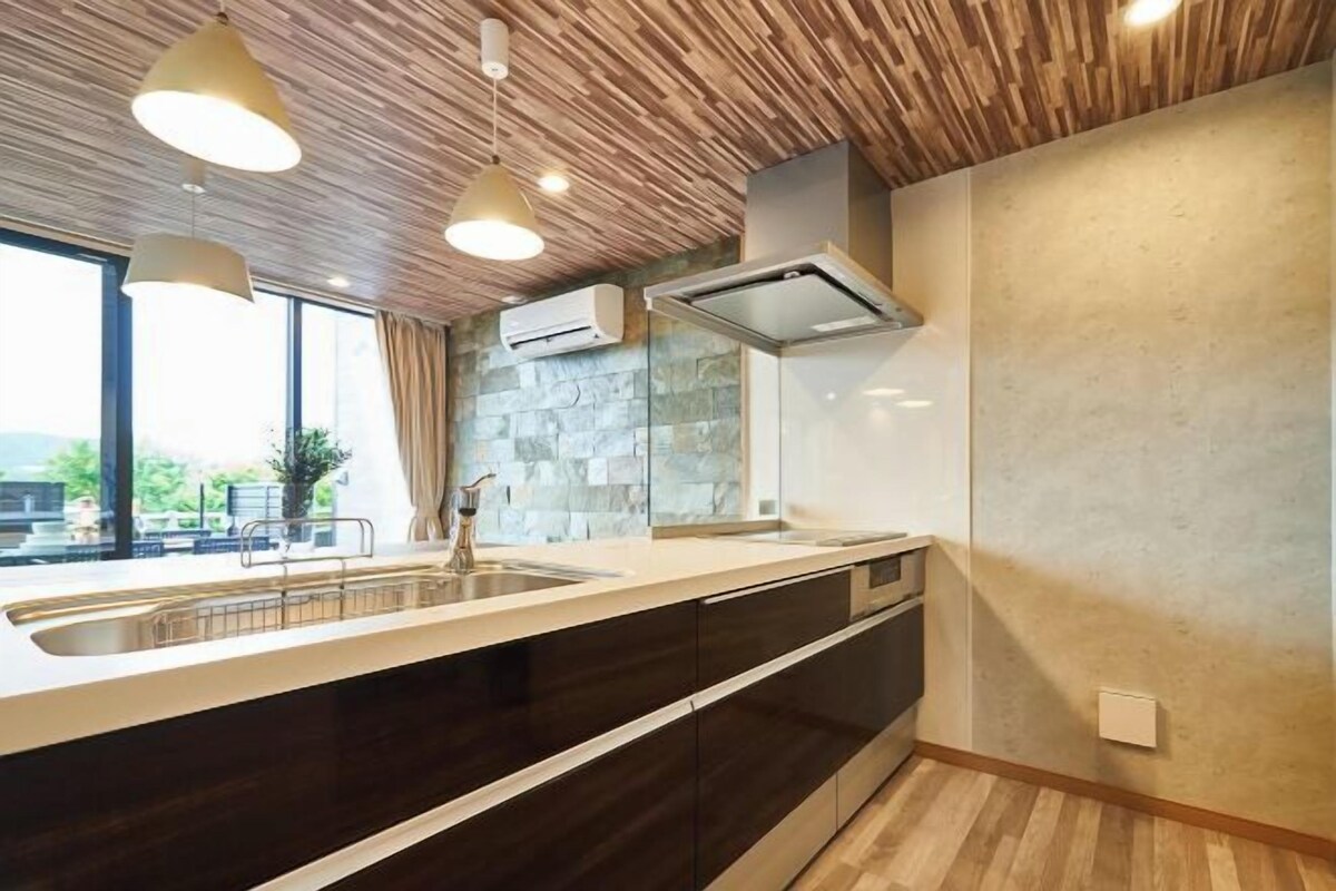 A modern kitchen with a wooden ceiling, a large window, and a stone backsplash.