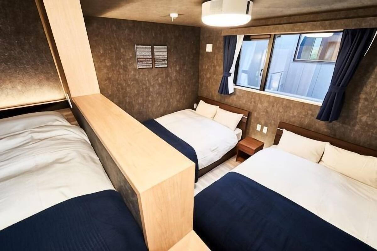 Habitación de hotel con dos camas, un banco de madera, una mesita de noche y un ventanal con cortinas.