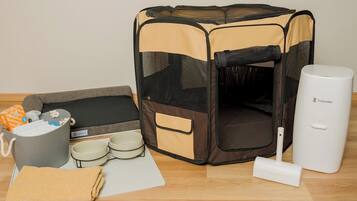 A pet bed, a waste bin, a water bottle, and a white device on a wooden floor.