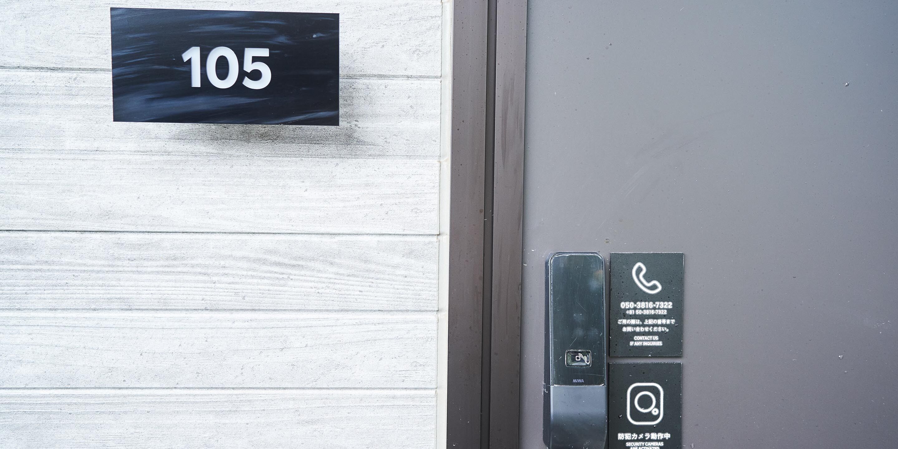 A door with a number sign '105' and a security camera panel with contact information.