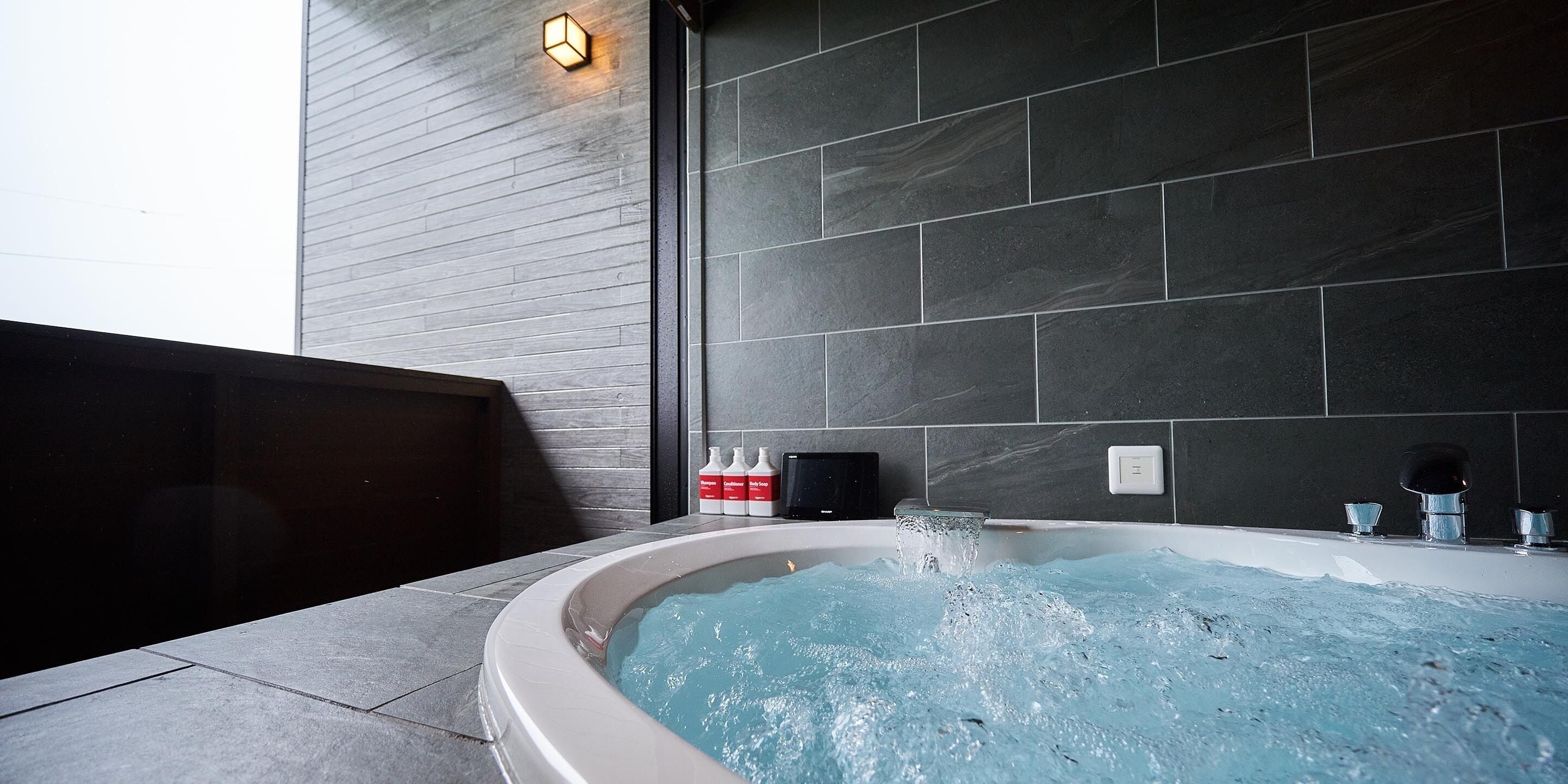 A modern bathroom with a freestanding bathtub, dark tiled walls, and a light fixture.