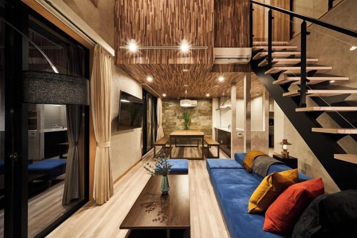 A modern interior with a wooden ceiling, a staircase, a sofa with colorful cushions, and a dining area.