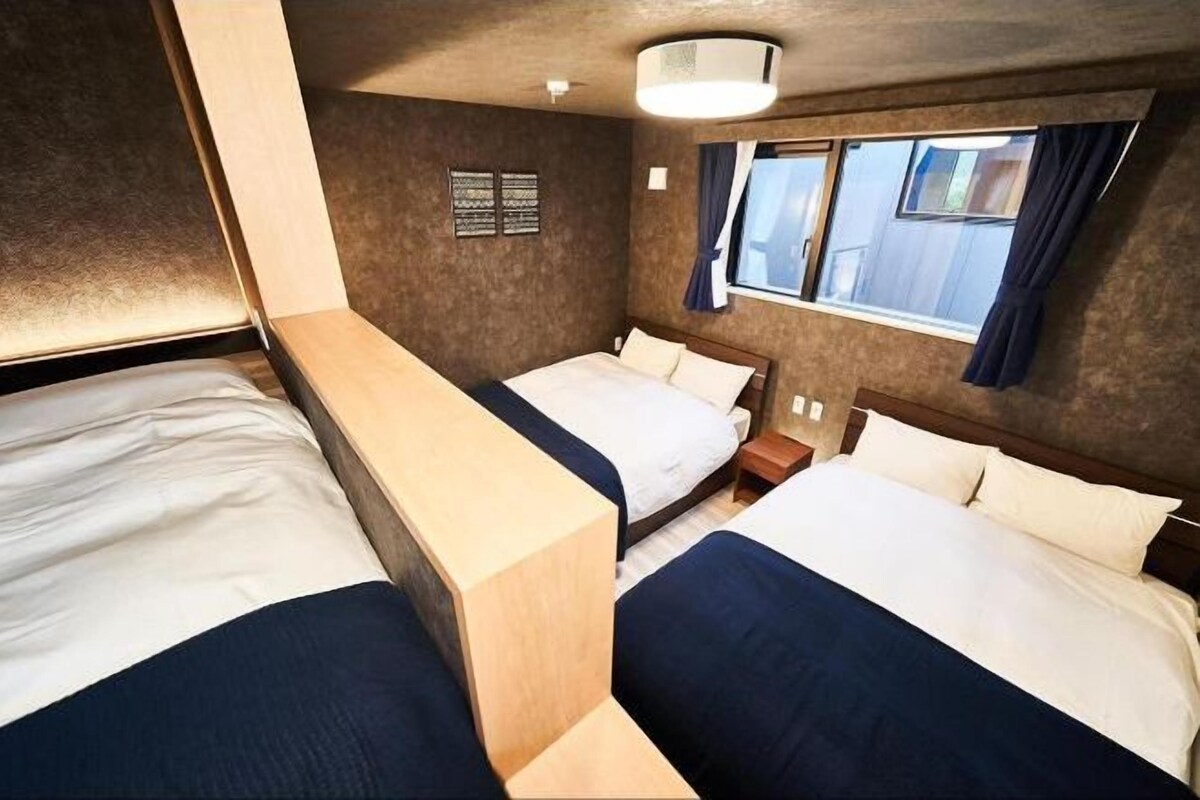 A compact hotel room with two beds, a small window with curtains, and a wall-mounted light fixture.