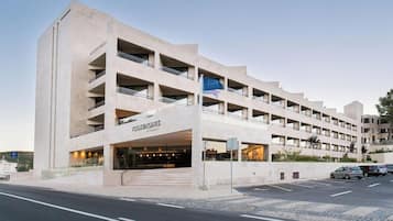 Ein mehrstöckiges Hotel mit modernem Design, das einen markanten Eingangsbereich und einen Parkplatz vor dem Gebäude aufweist.