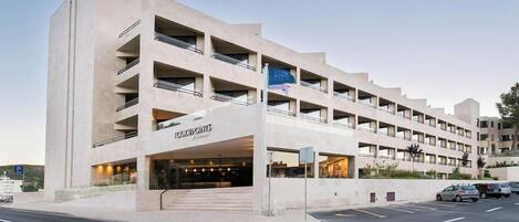 Un hotel de varios pisos con diseño moderno, que cuenta con una entrada destacada y un estacionamiento al frente.