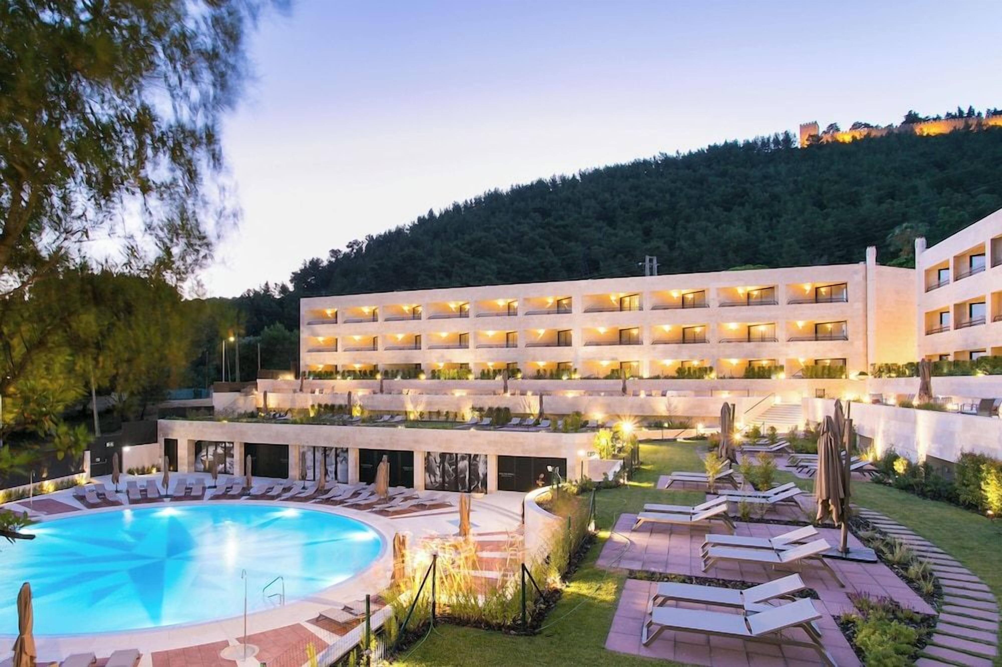 A hotel with a pool, outdoor seating, and a hillside backdrop.