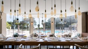 Spiseområde med udsigt til en pool, borde dækket med hvidt service og hængende lamper.