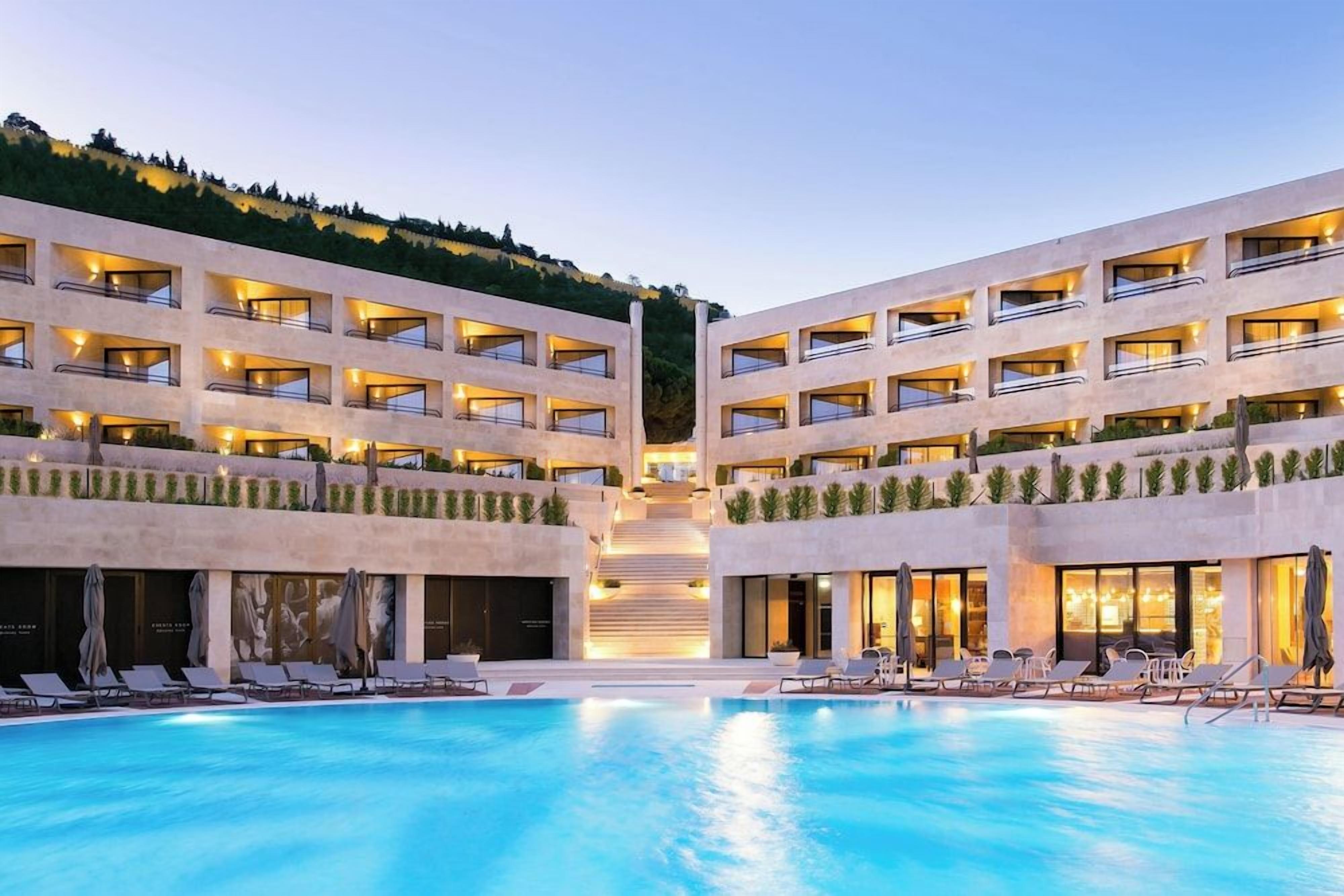 A hotel with a central pool, multiple balconies, and a landscaped terrace.