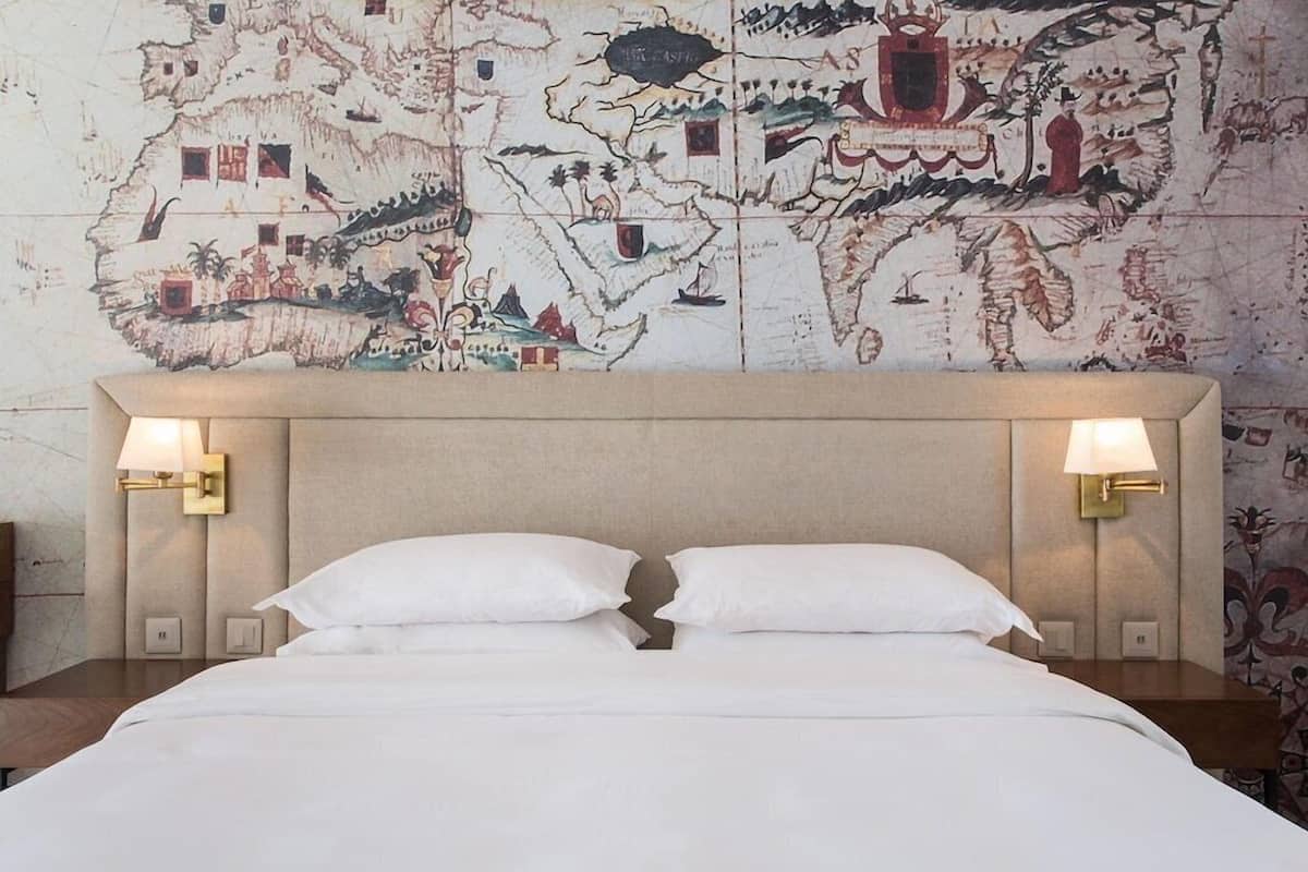A hotel room with a large bed, two bedside lamps, and a wall with a detailed map.
