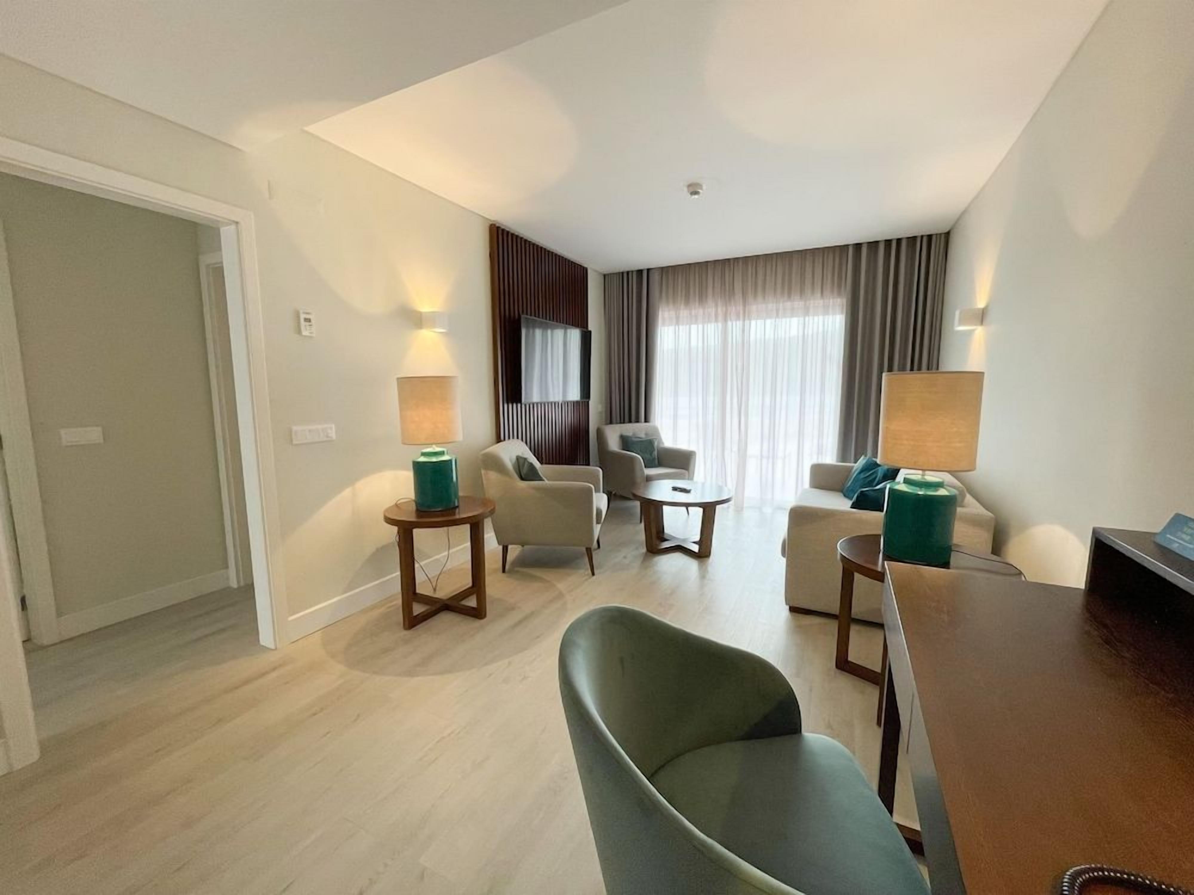 A modern hotel room with a dining area, a sofa set, and a television.