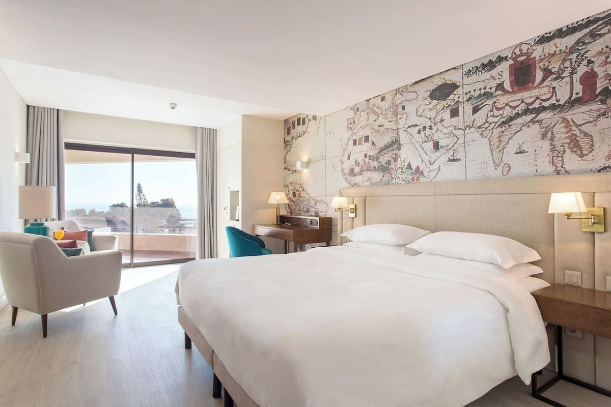 A hotel room with a large bed, a desk, a chair, and a view of the city.