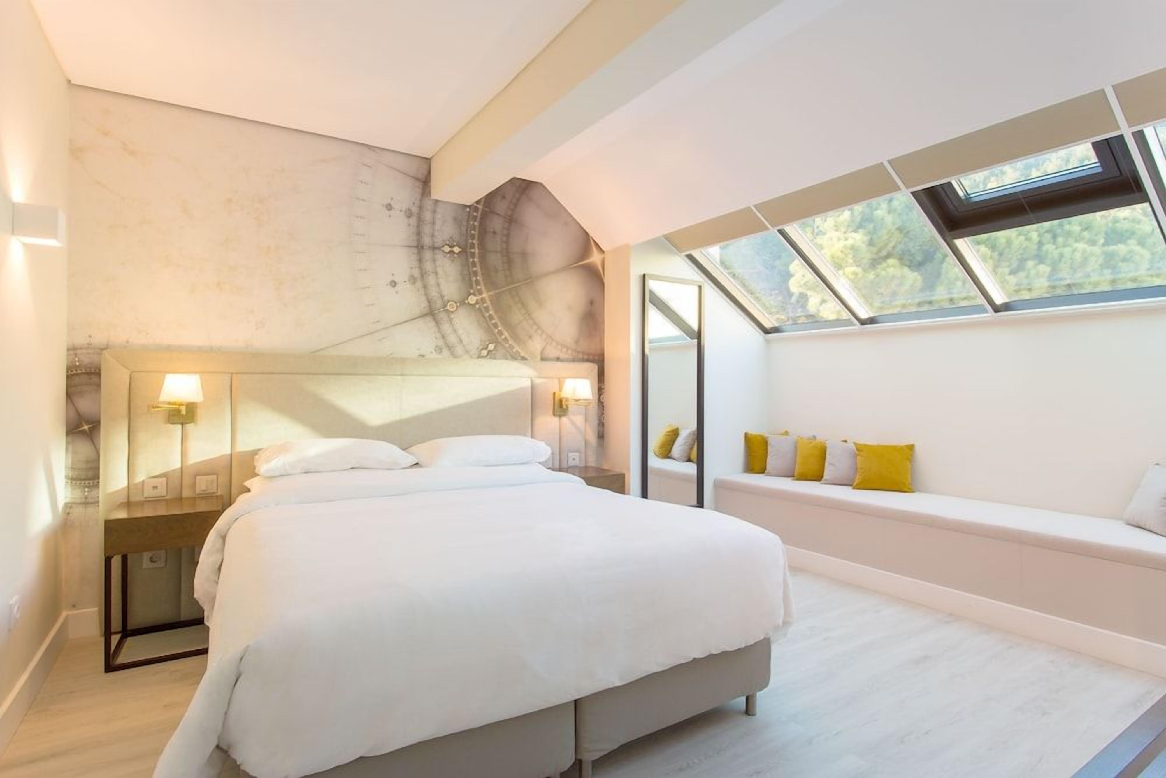 A bedroom with a bed, bedside tables, a window seat with cushions, and a skylight.