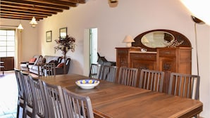 A dining area with a wooden table and chairs, a vase with flowers, and a cabinet with a mirror and lamp.