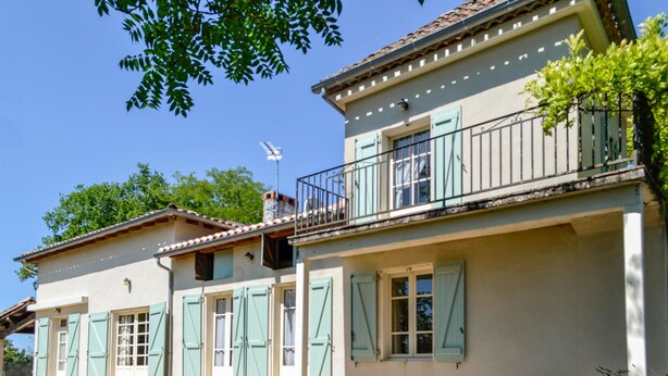 A two-story house with a balcony, shutters, and a satellite dish.