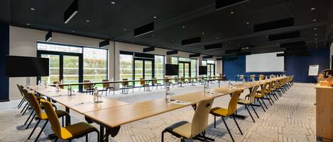 A conference room with long tables, yellow chairs, and a projector screen.