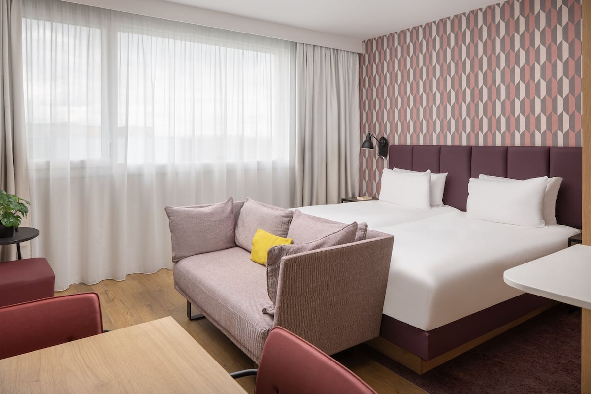 Une chambre d’hôtel avec un lit, un canapé, une petite table et une lampe.
