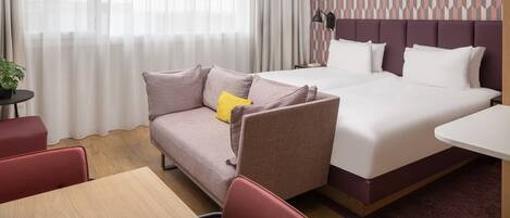 A hotel room with a bed, a sofa, a small table, and a lamp.