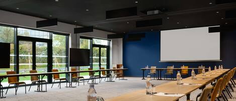 A conference room with long tables, chairs, water bottles, and a projector screen.