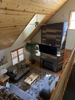 A cozy living room with a fireplace, wooden ceiling, and a large TV. - Family Fun Cabin In the Mountains (pinetop)