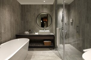 Un baño moderno con una bañera independiente, un espejo redondo, un lavabo con encimera oscura y zona de ducha con mampara de cristal.