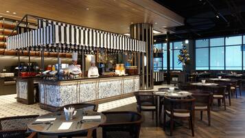 A modern restaurant with a central bar area, multiple dining tables, and chairs.
