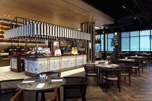 A modern restaurant with a central bar area, multiple dining tables, and chairs.