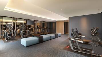 A modern gym with various exercise equipment, a seating area, and a large mirror.