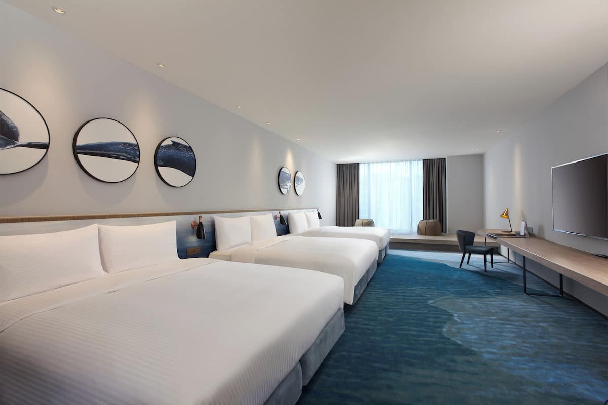 Una habitación de hotel con tres camas, un escritorio, una silla y un televisor.