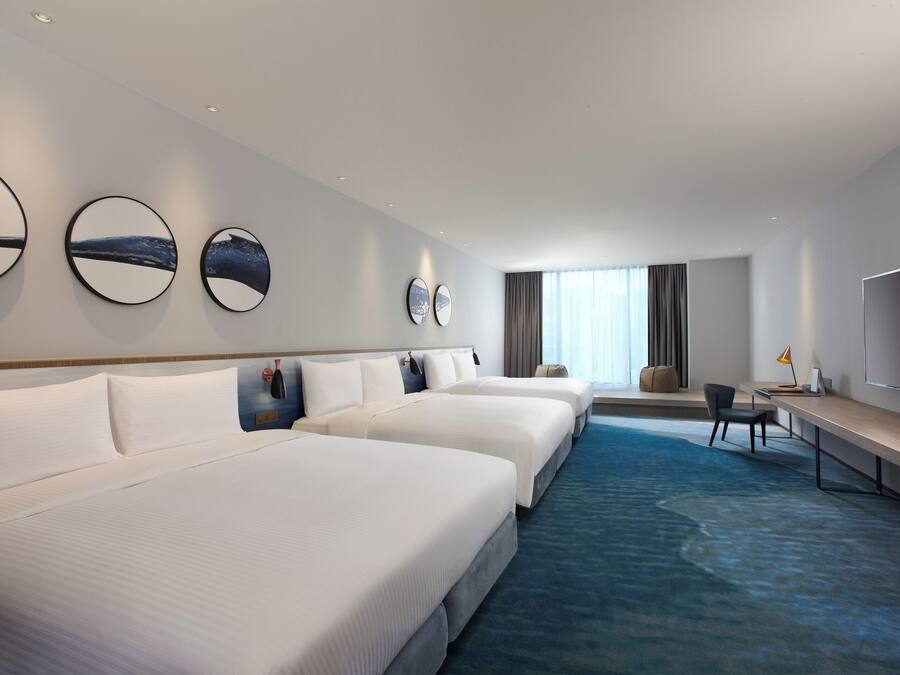A hotel room with three beds, a desk, a chair, and a TV.