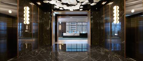 A modern lobby with a marble floor, a reception desk, and a ceiling with hanging light fixtures.