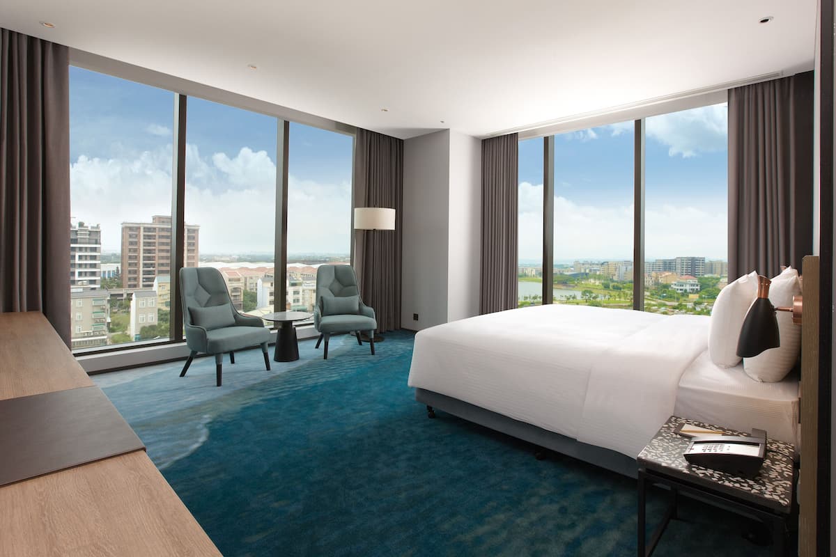 Habitación de hotel con una cama grande, dos sillones, una mesita y vistas a la ciudad.