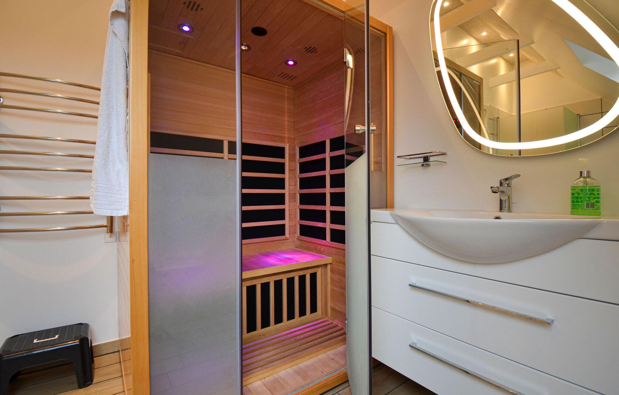 Une salle de bain moderne avec un sauna en bois, un lavabo blanc et un miroir doté d’un cadre éclairé.