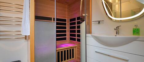 Une salle de bain moderne avec un sauna en bois, un lavabo blanc et un miroir doté d’un cadre éclairé.