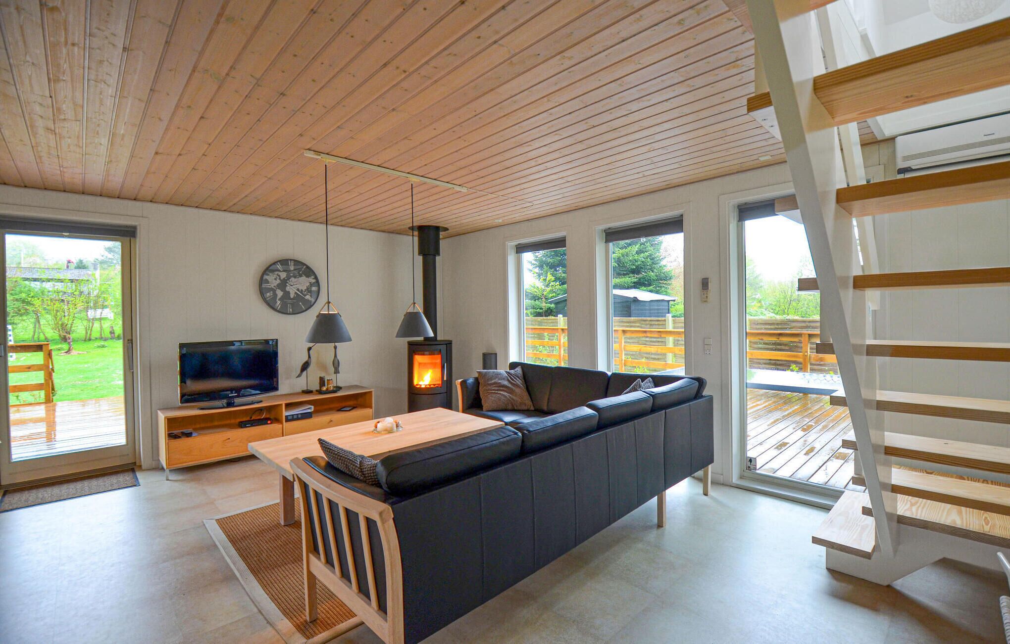 Un soggiorno moderno con soffitto in legno, un divano spazioso, una televisione, un camino e ampie finestre.
