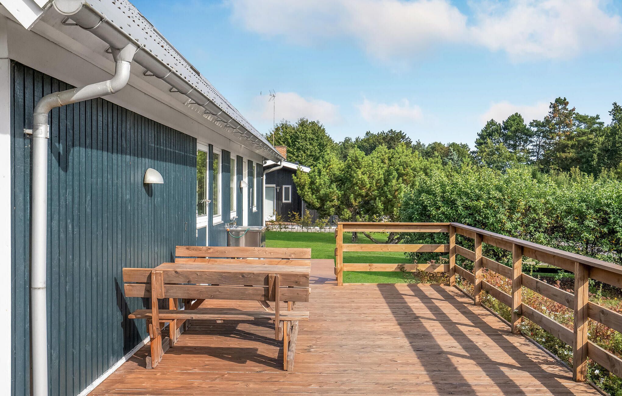 Une terrasse en bois avec un banc, une rambarde et un bâtiment doté de fenêtres et d’une porte.