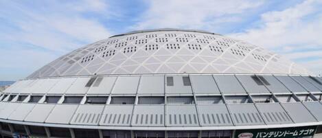 A large, modern stadium with a dome roof and a commercial building labeled "Kowa Panterland Nagoa" in front.