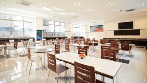Una cafetería espaciosa con varias mesas y sillas, ventanas amplias y un televisor montado.