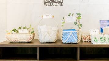 A reception area with a 'WELCOME' sign, three baskets labeled 'Razor', 'Comb', and 'Green Tea', and a 'Toyoko Inn' brochure.