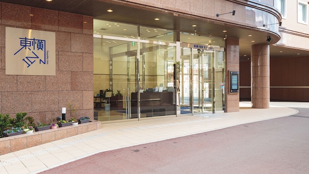 Entrada de un hotel con un letrero que dice "Toyoko Inn" y puerta de acceso de vidrio.