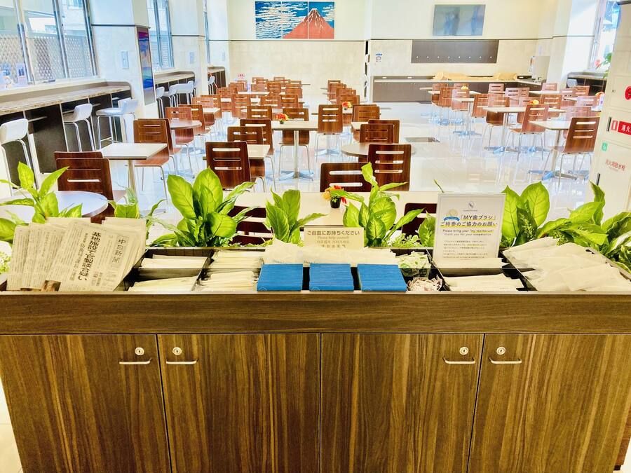 A spacious dining area with multiple tables and chairs, a reception desk with informational brochures, and a large window providing a view of the outside.