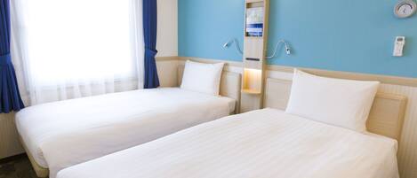 Une chambre d’hôtel avec deux lits, une fenêtre avec des rideaux, une horloge murale et une étagère contenant des articles de toilette.