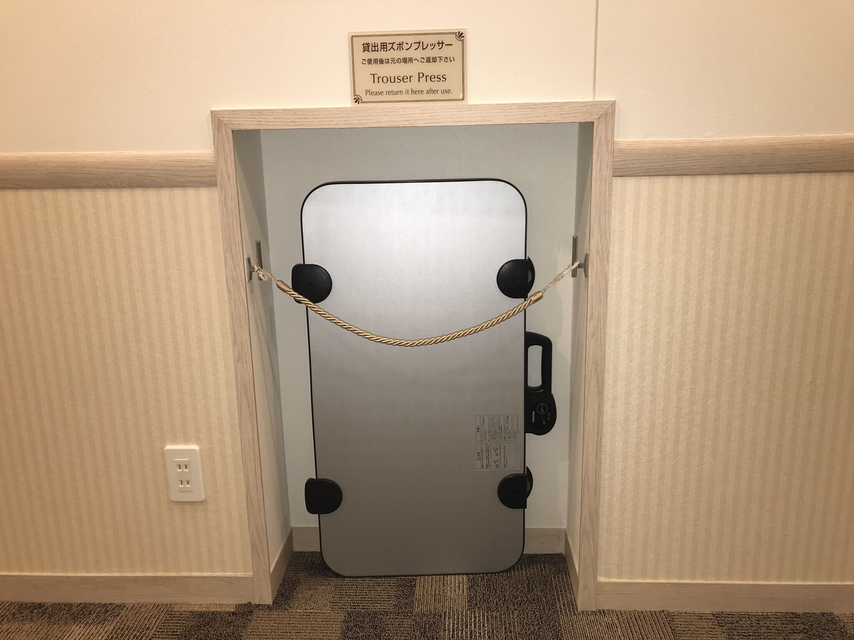 Una puerta con un letrero que indica devolverla después de usarla, una barrera de cuerda y un enchufe en la pared.