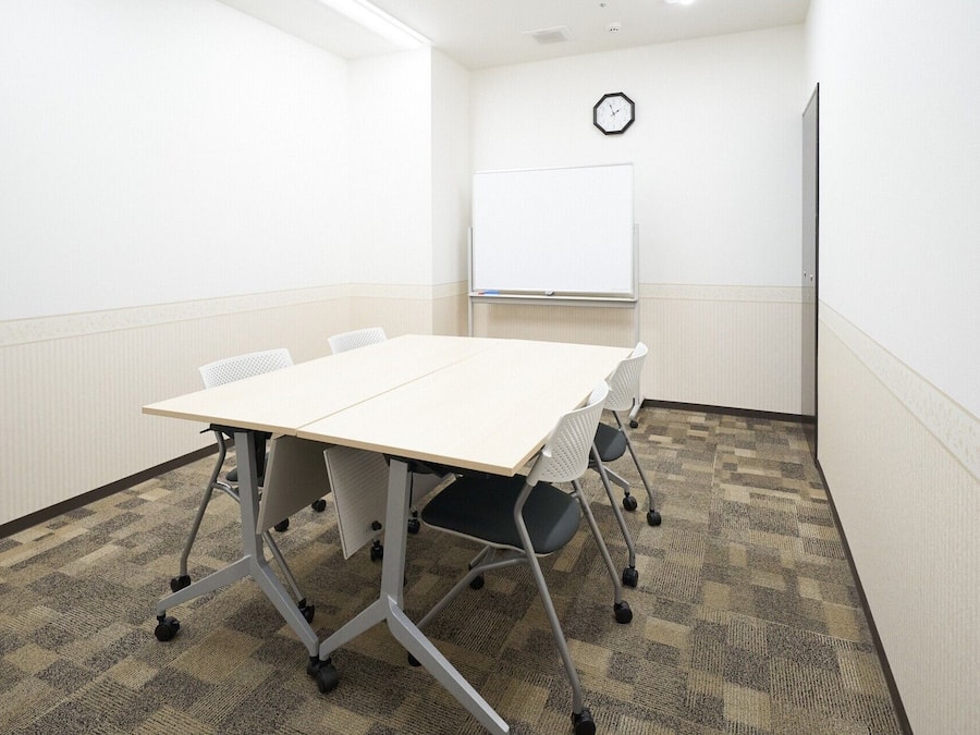 Un salón de conferencias con una mesa blanca, cuatro sillas, una pizarra y un reloj en la pared.