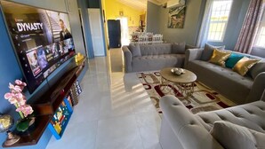 Un espacio habitable amplio con televisor de pantalla plana, un sofá, una mesa de centro y una zona de comedor al fondo.