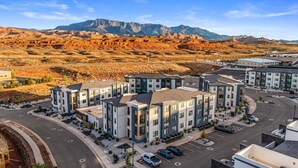 A modern apartment complex with multiple buildings, a parking lot, and a mountainous backdrop. - B6, Hillside Hideaway, Indoor and Outdoor Fireplace, Community Amenities, Near Sand Hollow (Hurricane)