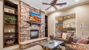 A living room with a stone fireplace, a ceiling fan, and a large window with blinds. - B6, Hillside Hideaway, Indoor and Outdoor Fireplace, Community Amenities, Near Sand Hollow (Hurricane)